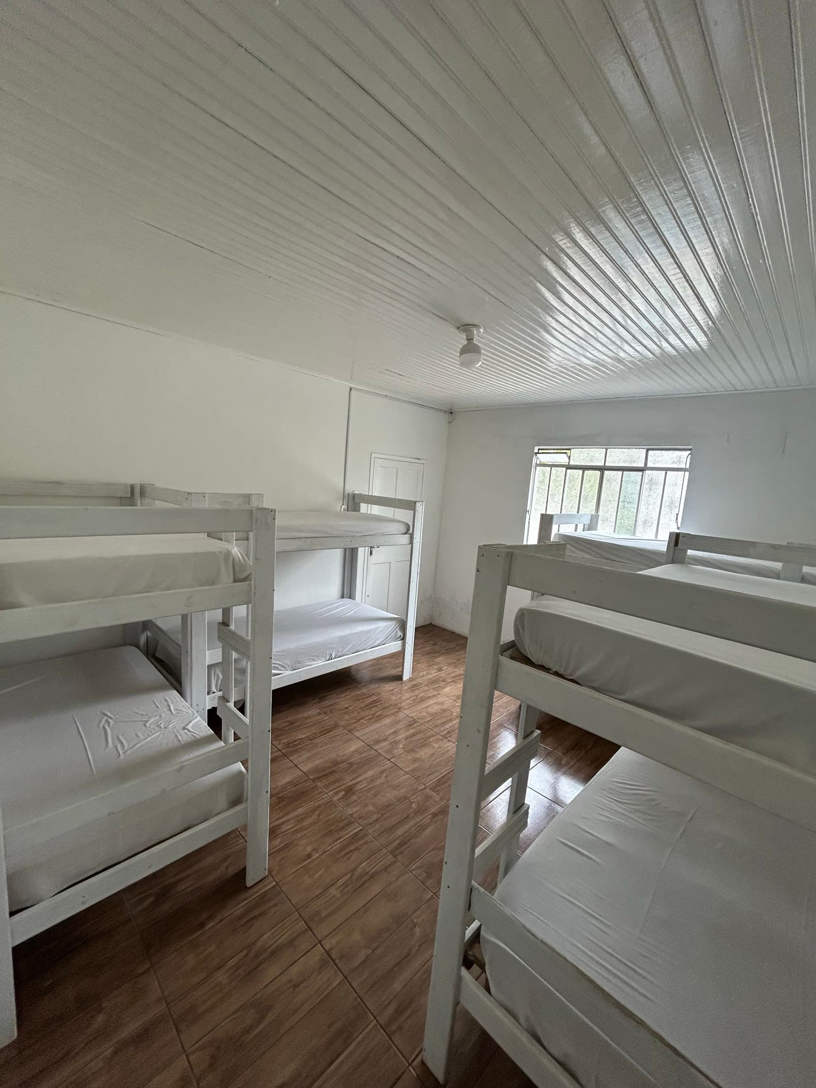 Beliches brancos alinhados em quarto amplo com janela ao fundo