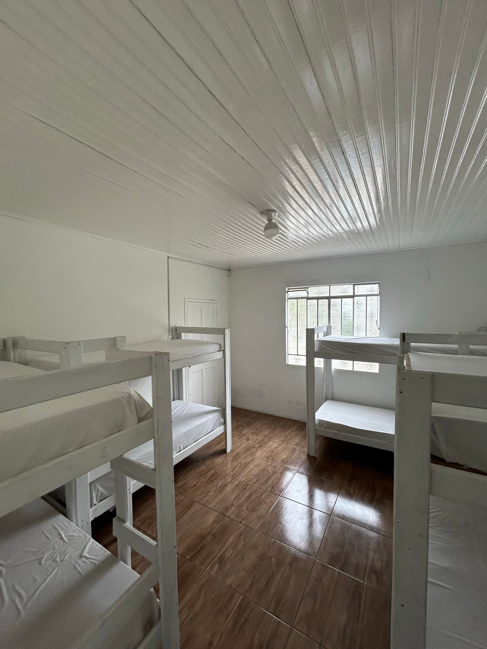 Quarto da ala nova com beliches brancos e forro de madeira pintado